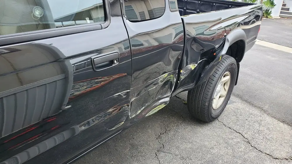 Pickup truck rear door and bed panel buckled, with paint transfer from a collision