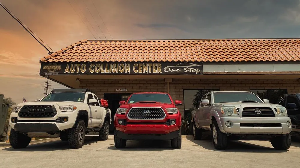 Three Toyota Tacoma pickups lined up under the One Stop Auto Collision Center sign